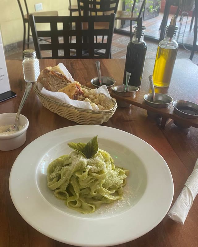 Mesa puesta con fettuccine al pesto, pan de la casa y aceite de oliva